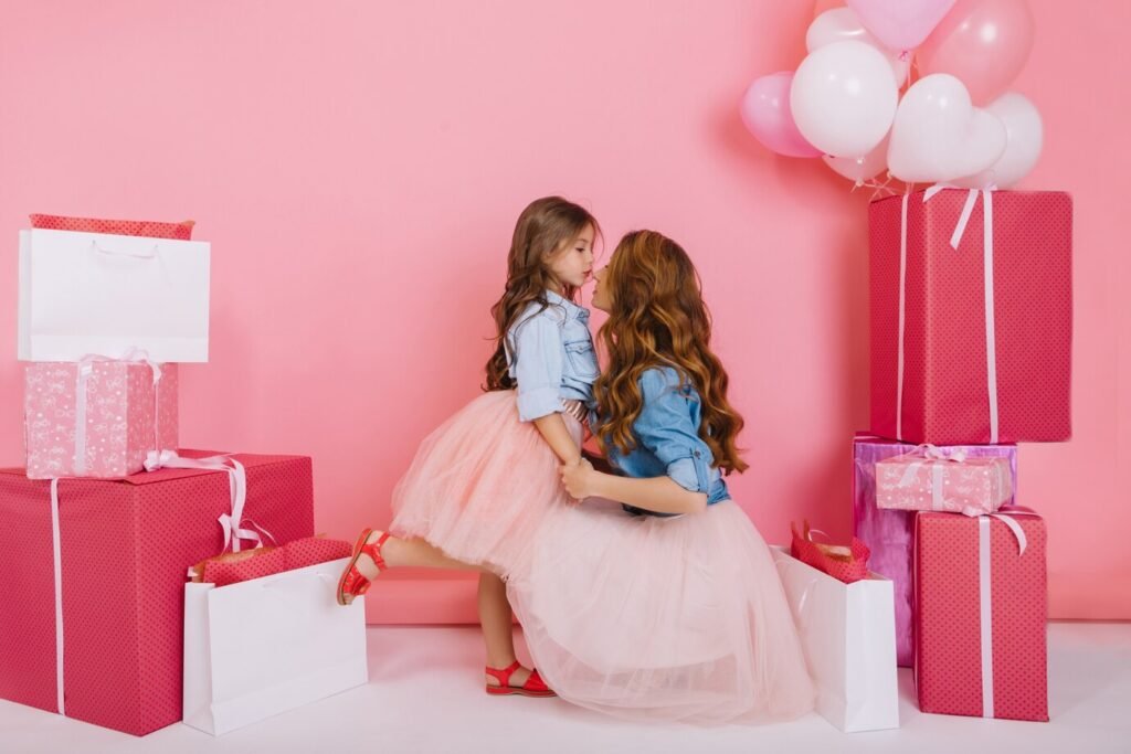 Imagem de uma mãe com sua filha, em um espaço decorado com presentes e balões rosa, remetendo ao Dia das Mães
